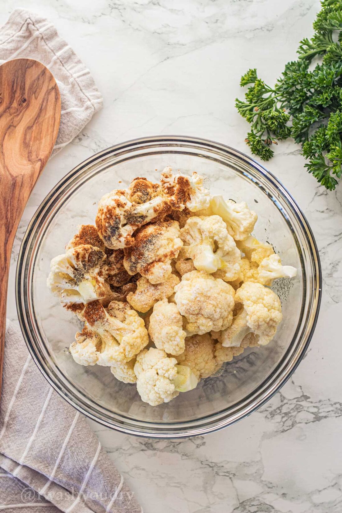 Bowl of raw cauliflower with spices and olive oil in it. 