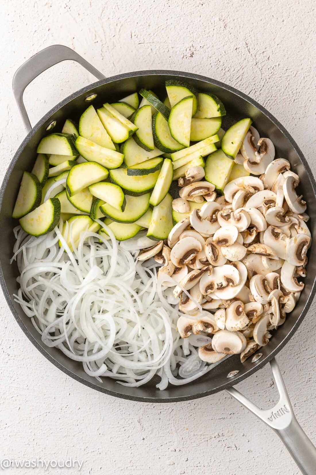 Raw zucchini, mushrooms, and onions in a frying pan. 