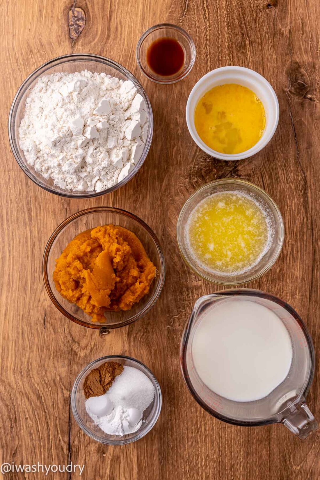 Ingredients for pumpkin pancakes in glass bowls on wooden surface. 
