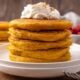 stack of pumpkin pancakes on white plate with whipped cream on top.