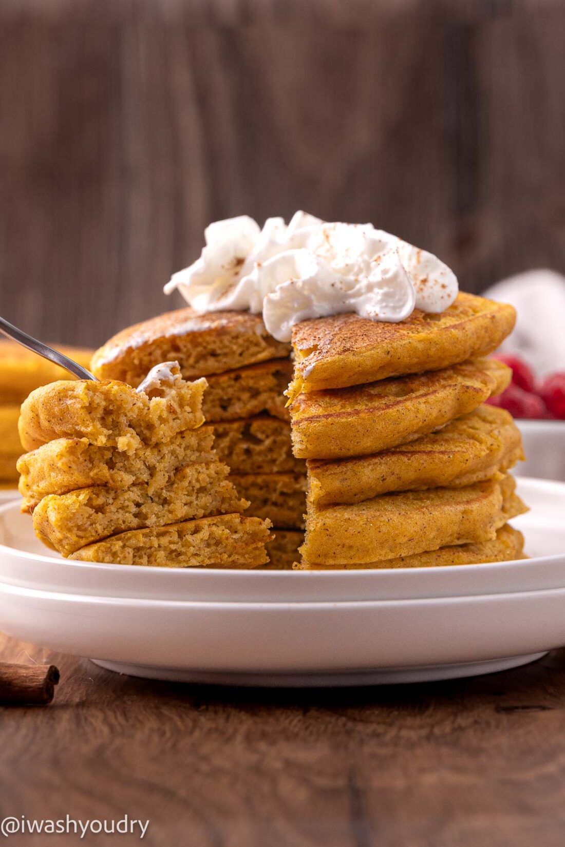 Stack of fluffy pumpkin pancakes with bite removed on white plate. 