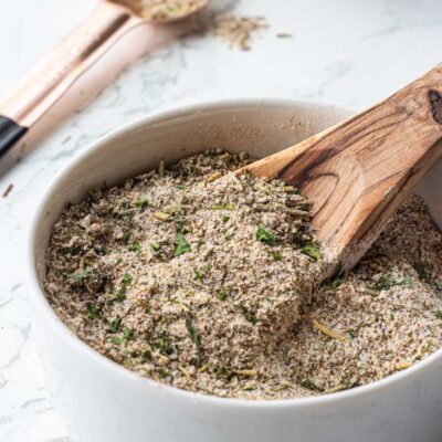 Greek spice blend with wooden spoon in white bowl.
