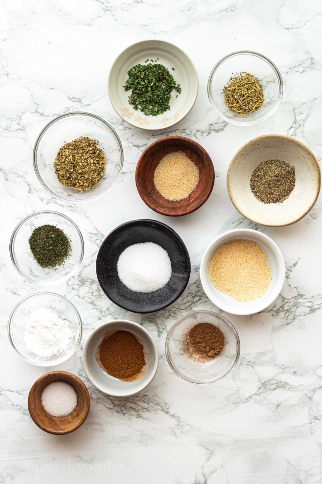 12 spices in glass bowls on marble countertop. 