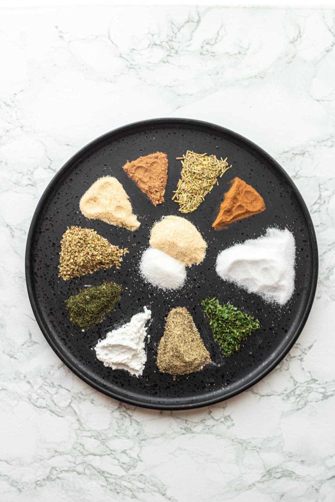 12 spices in triangle shape on black plate. 