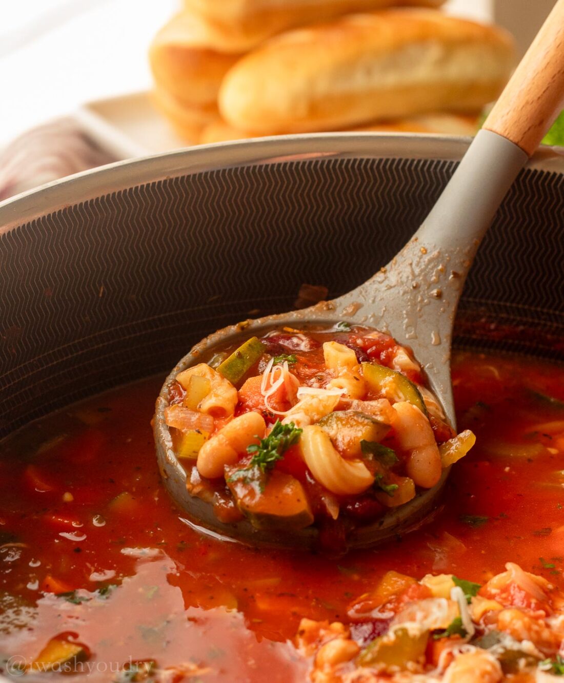 ladle filled with minestrone soup and beans with pasta.