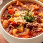 white bowl filled with minestrone soup and beans with parmesan cheese on top.