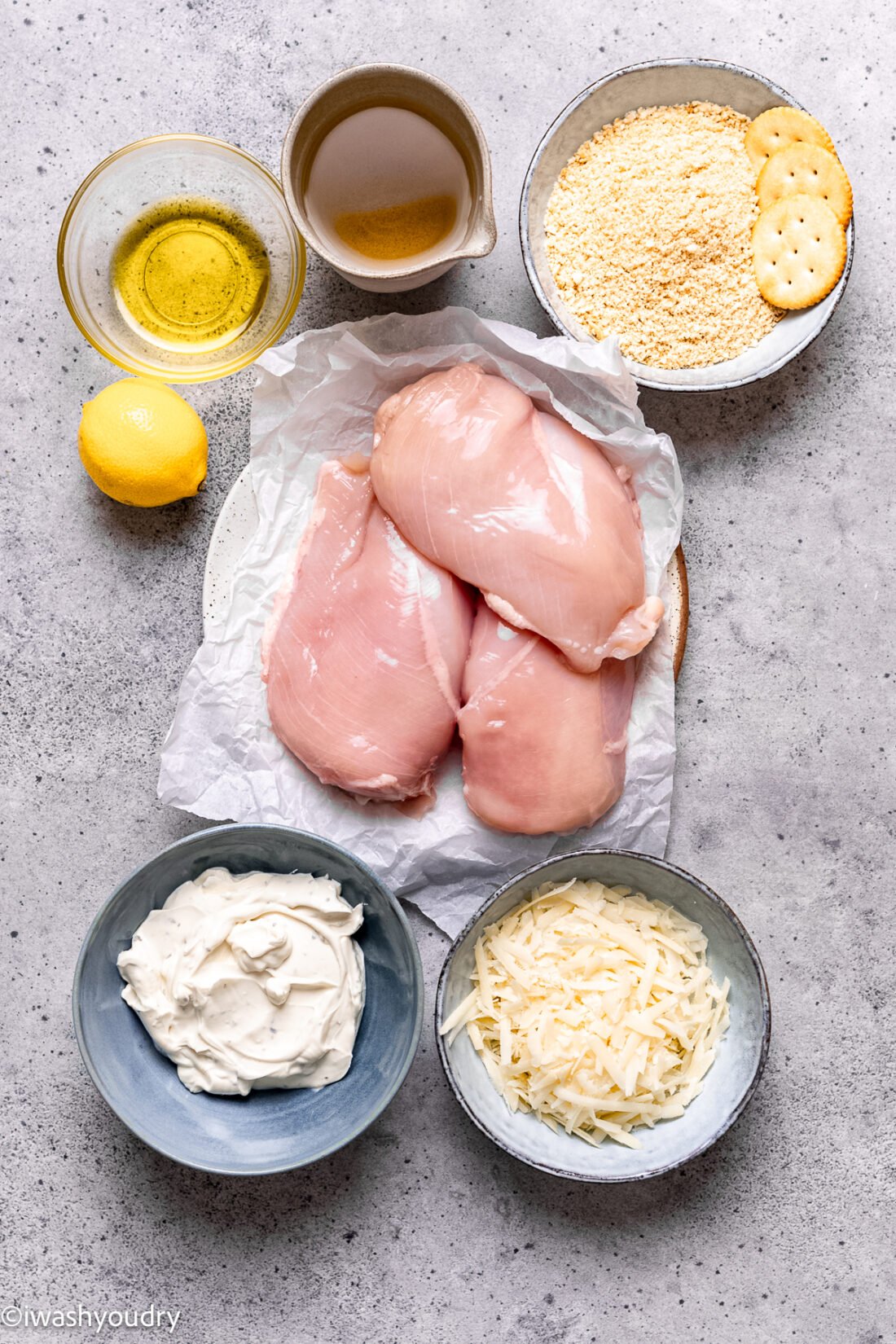 Raw ingredients for parmesan crusted chicken in dishes on concrete countertop. 