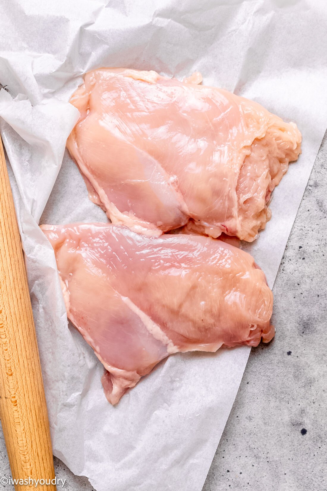 Raw chicken breasts on parchment paper with rolling pin. 