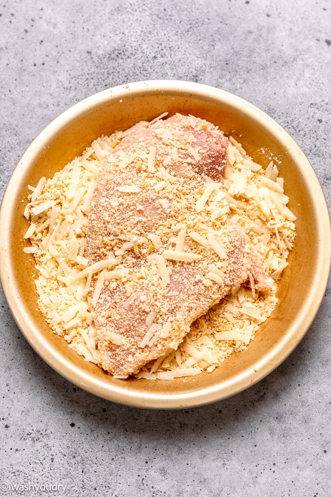 Raw chicken breast coated in parmesan cheese and cracker crumbs in a bowl. 