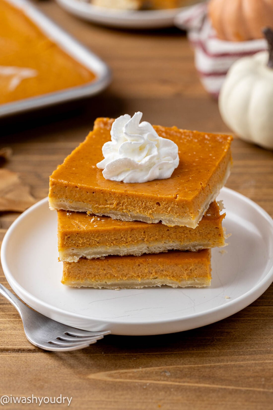 Stack of 3 pumpkin pie bars on a white plate with a fork. 