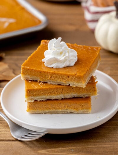 Stack of 3 pumpkin pie bars on white plate with fork.