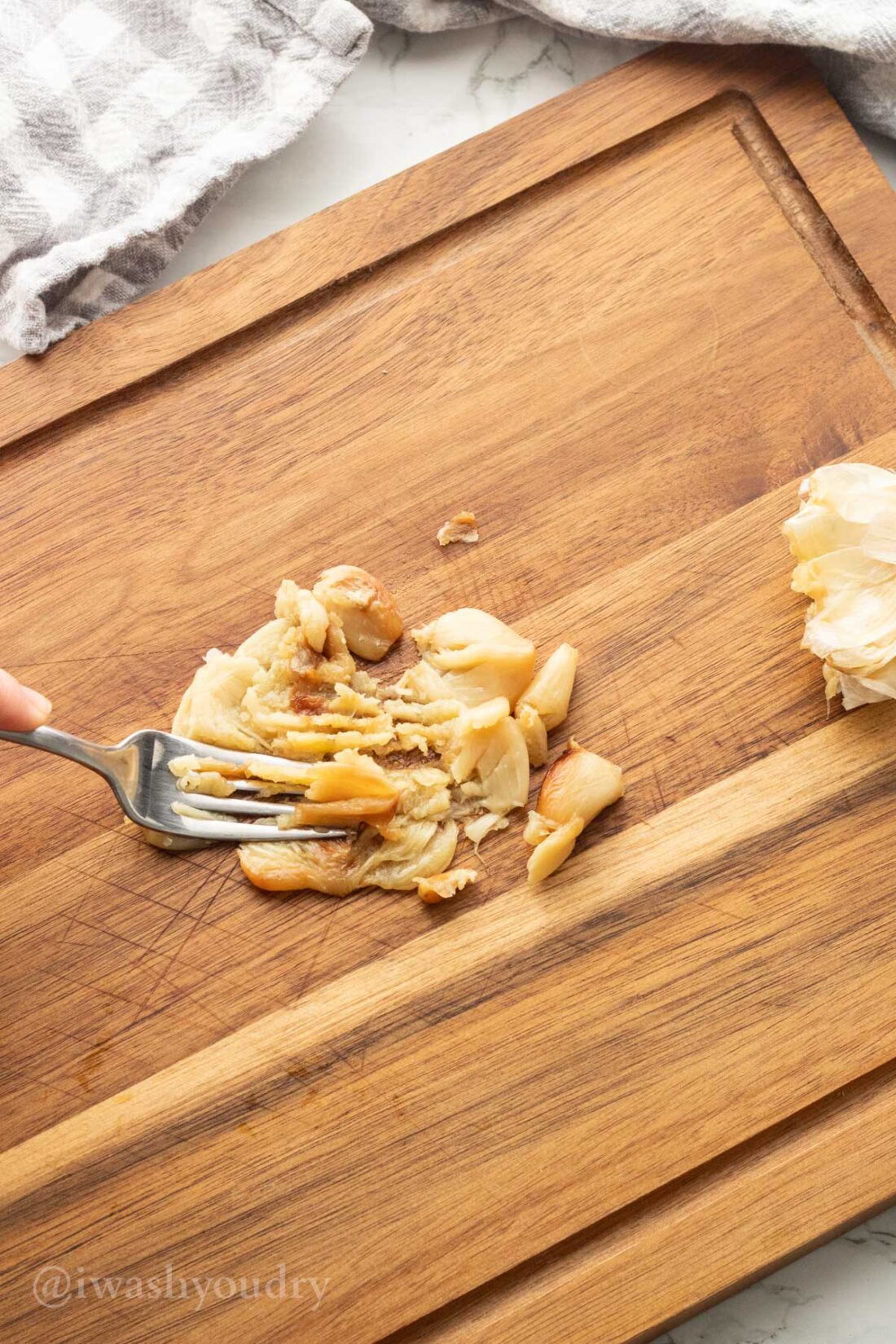 Fork mashing roasted garlic on wood cutting board. 