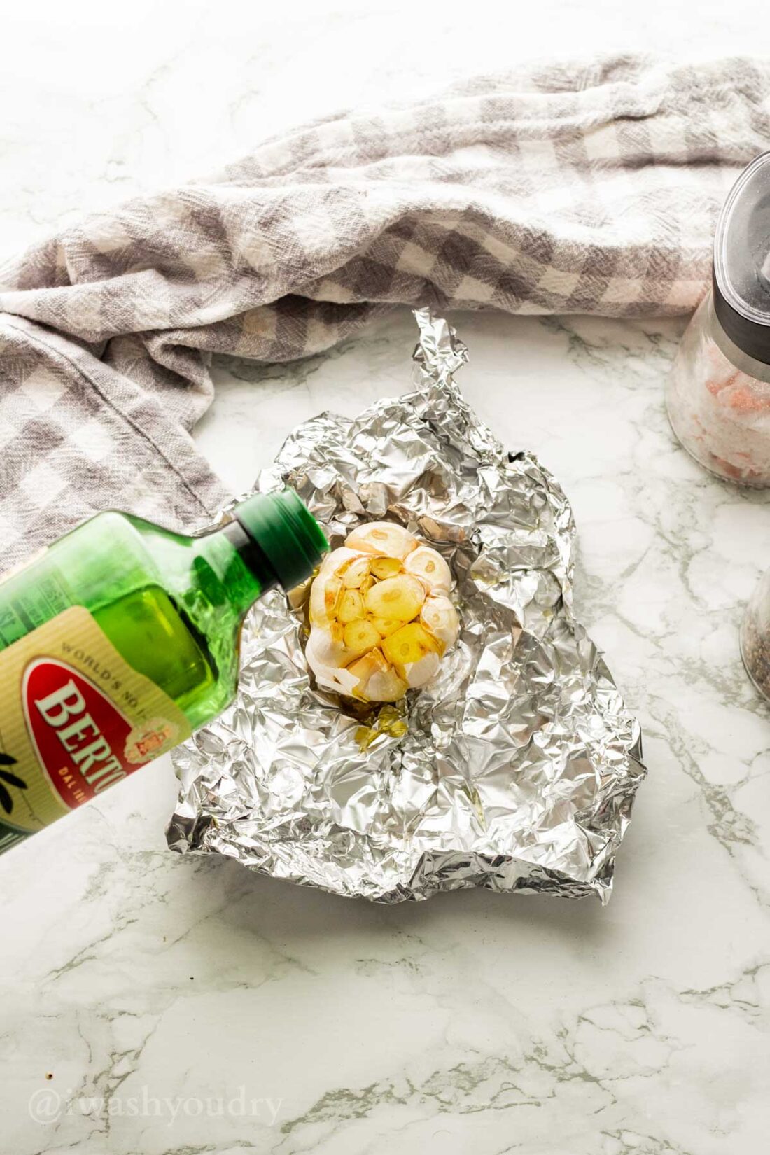 Pouring olive oil on head of garlic in tin foil on marble countertop. 