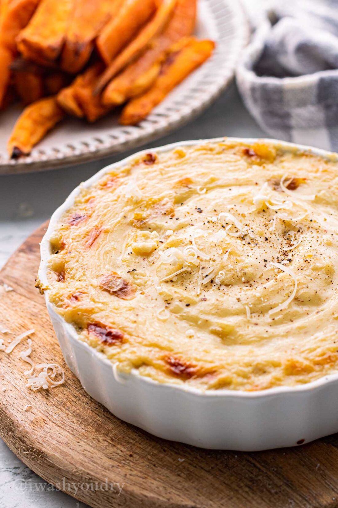 Baked roasted garlic dip with sweet potato fries in a white dish. 