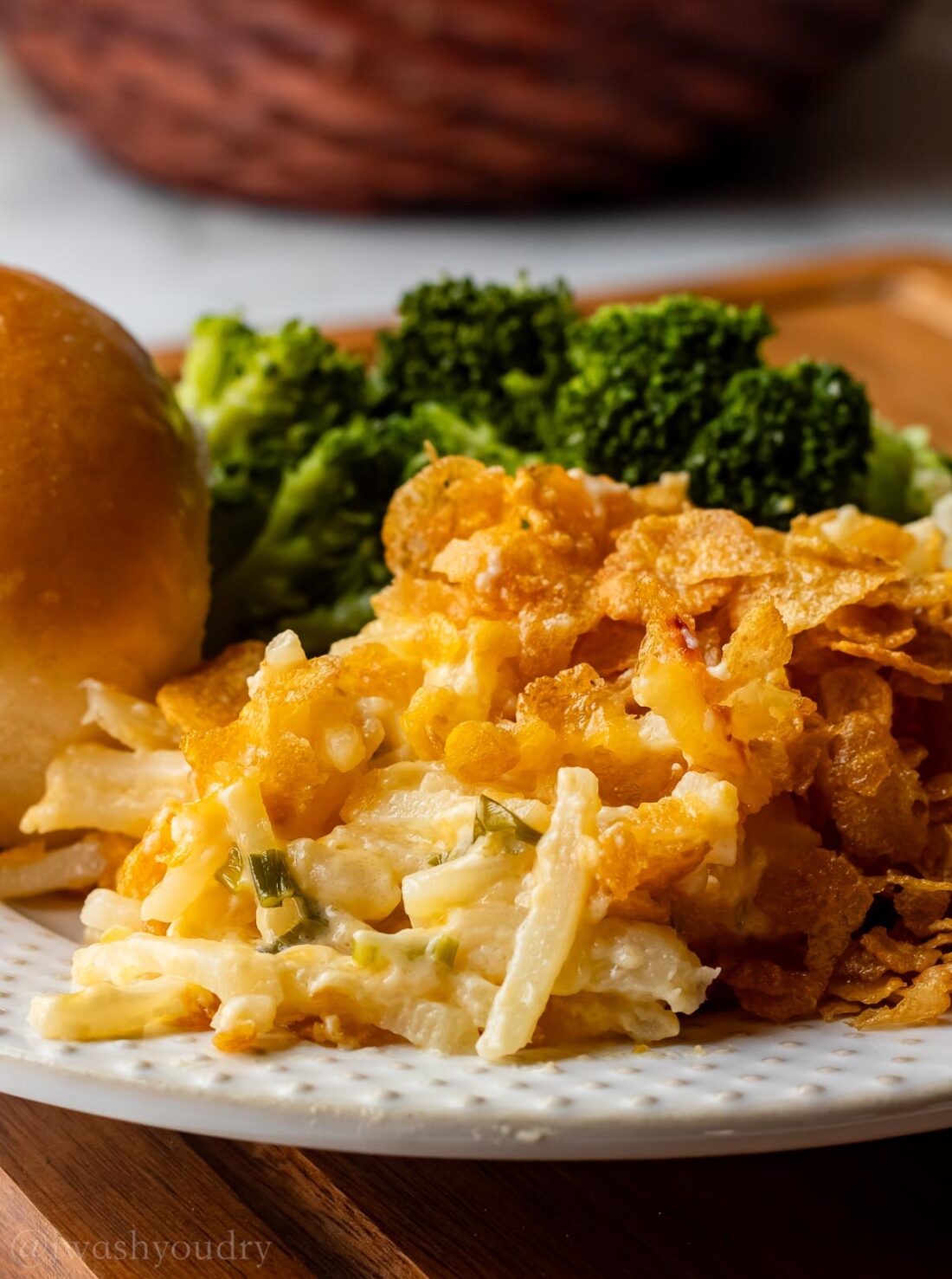 plate of cheesy potato casserole with roll and broccoli on the side.