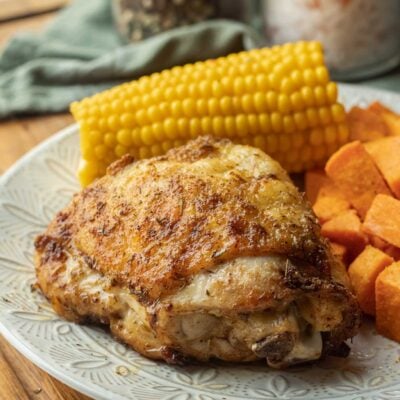 Cooked chicken thigh on white plate with corn and sweet potato.