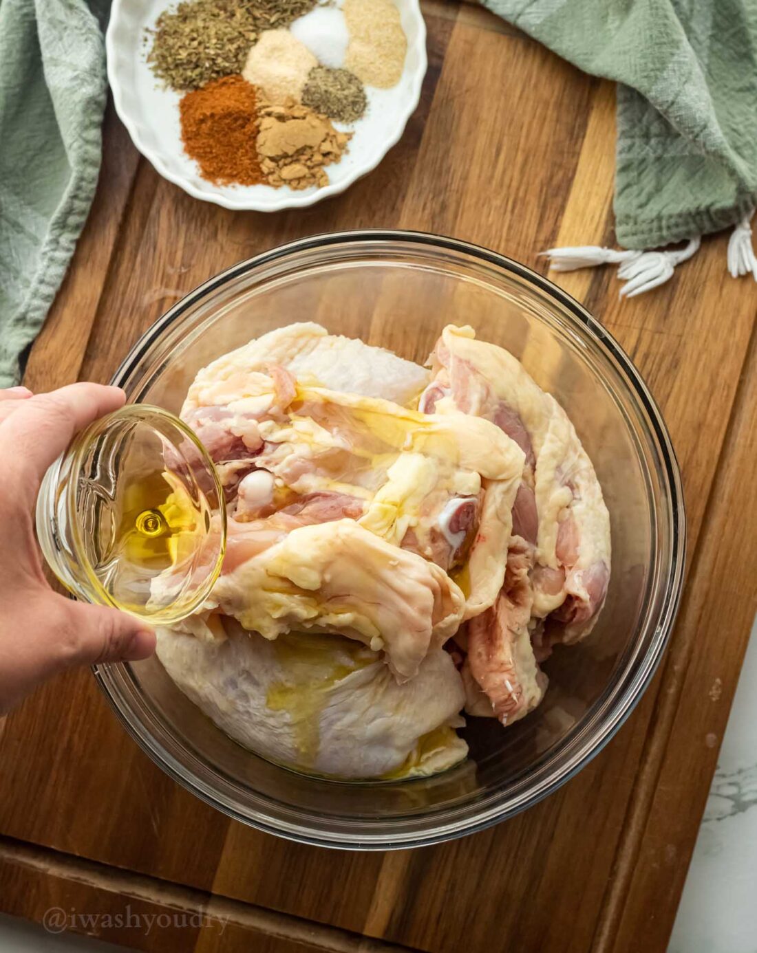 Raw chicken thighs in a glass bowl with hand pouring olive oil on top. 