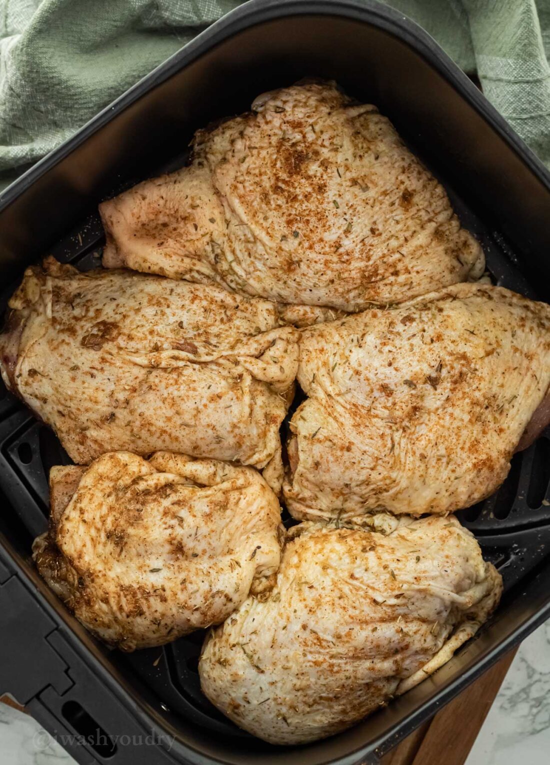 Raw chicken thighs in basket of air fryer, touching but not overlapping. 