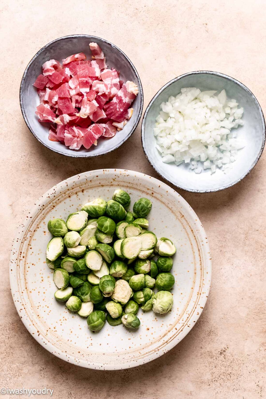 Ingredients for bacon and brussels sprouts in bowls on marble countertop. 