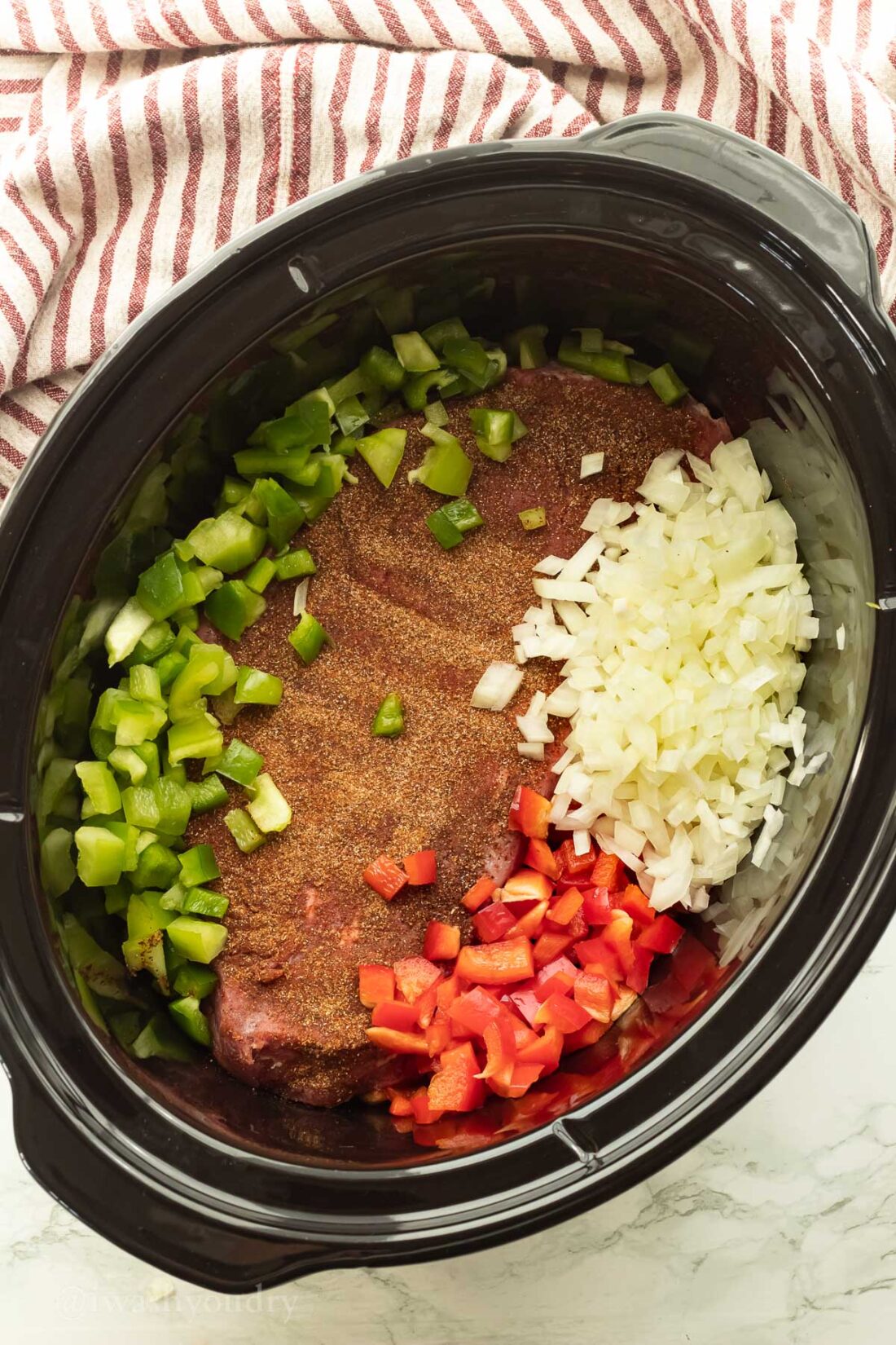 Raw flank steak, onions, and peppers in slow cooker bowl. 