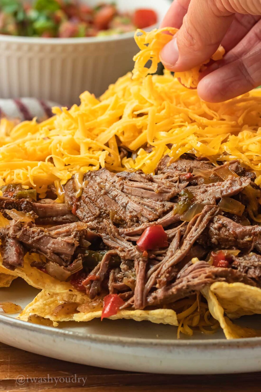 Hand sprinkling cheese over carne asada and chips on white plate. 