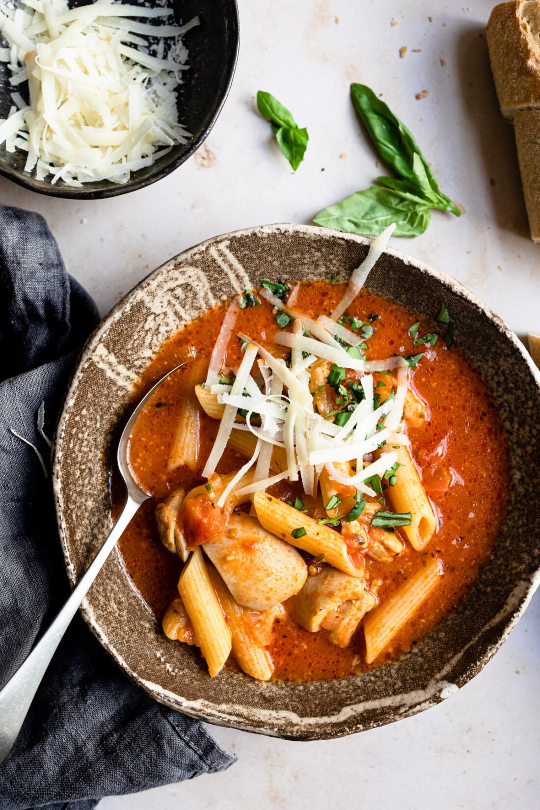 bowl of tomato soup with chicken, pasta and parmesan cheese on top.