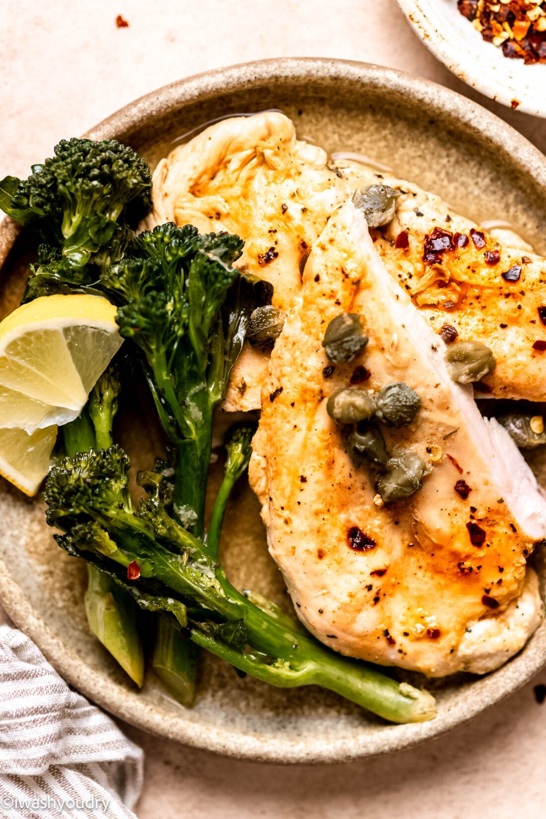 Cooked lemon chicken with broccolini on plate with lemon wedges.