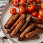 Cooked breakfast sausage on white plate with vine tomatoes.