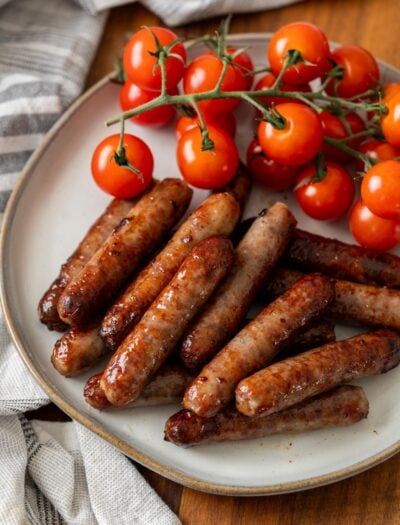 Cooked breakfast sausage on white plate with vine tomatoes.
