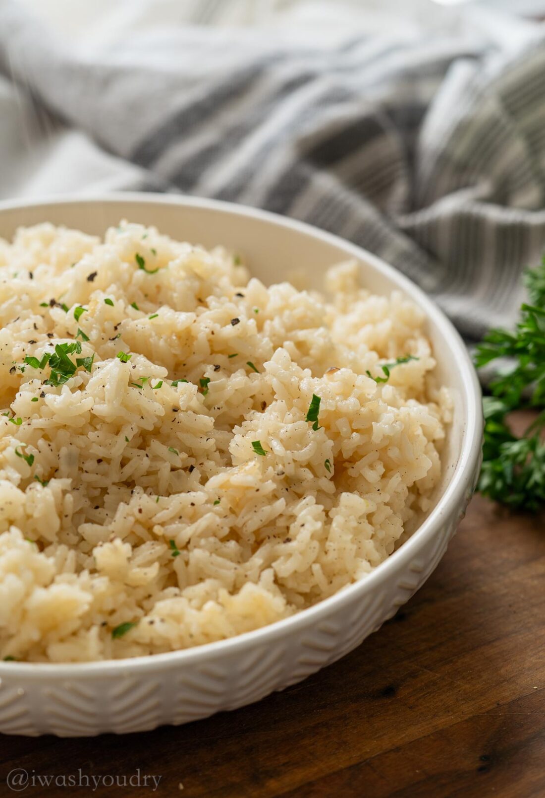 Cooked white butter rice pilaf in white textured bowl with parsley on top. 