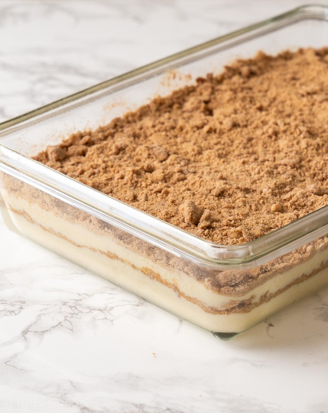 Raw coffee cake batter with brown sugar topping in glass pan. 