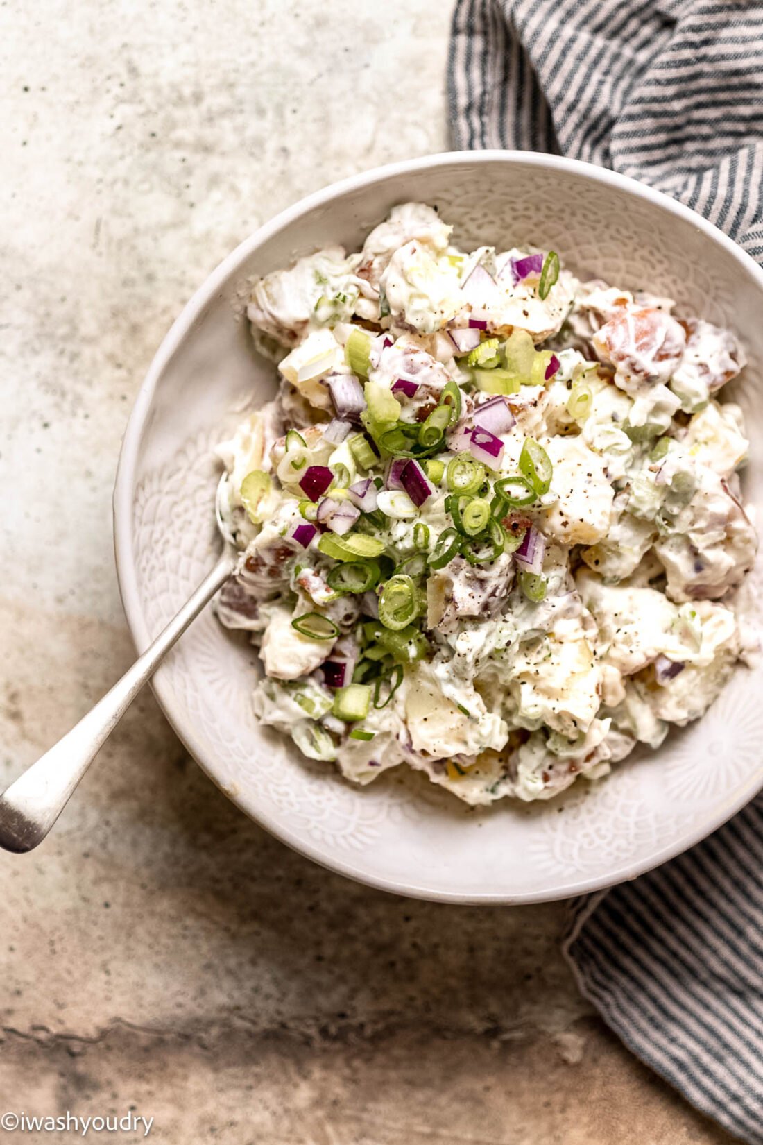 Creamy red potato salad in bowl with spoon and dish towel on the side. 