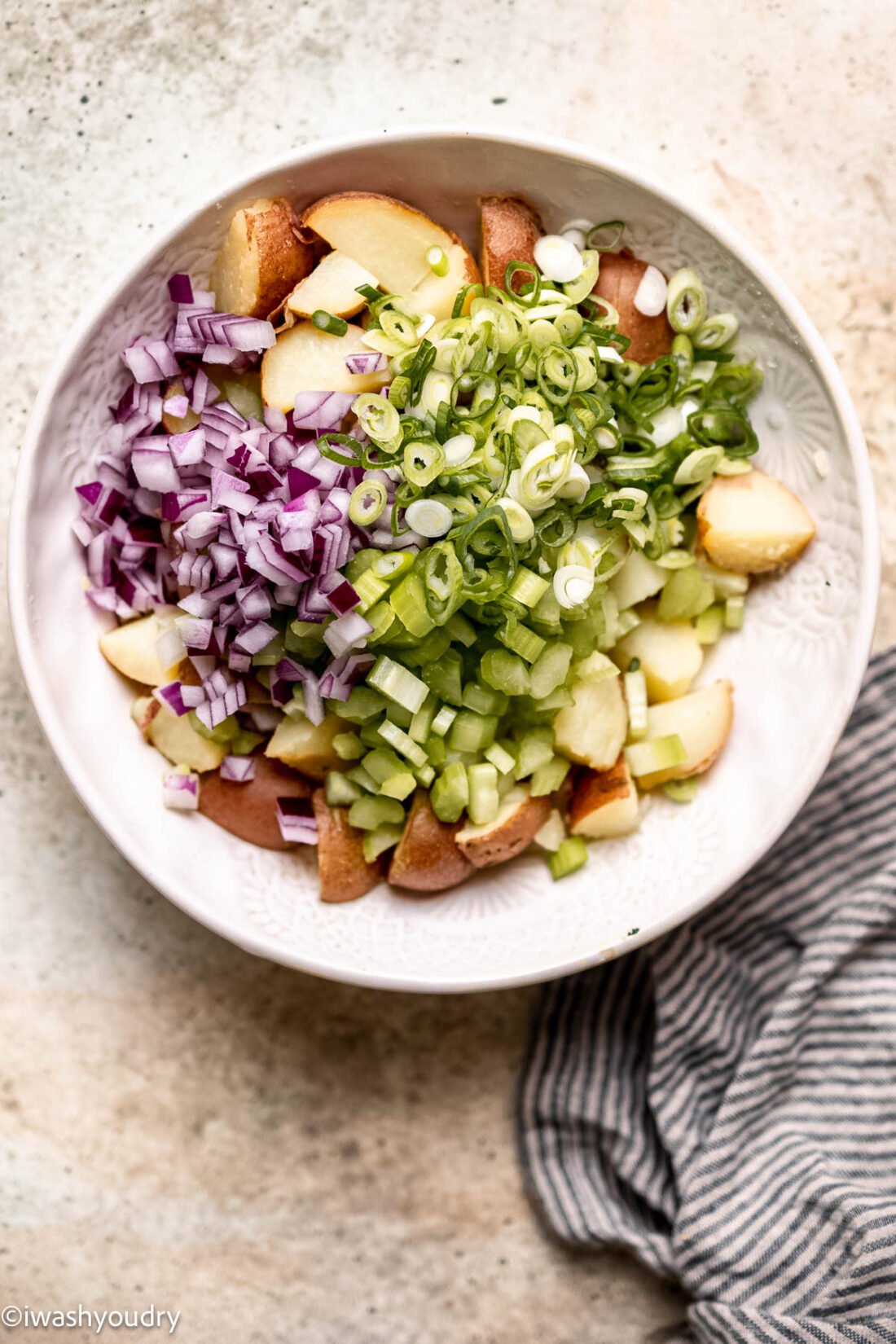 Red onion, celery, scallions, and cooked red potatoes in bowl. 