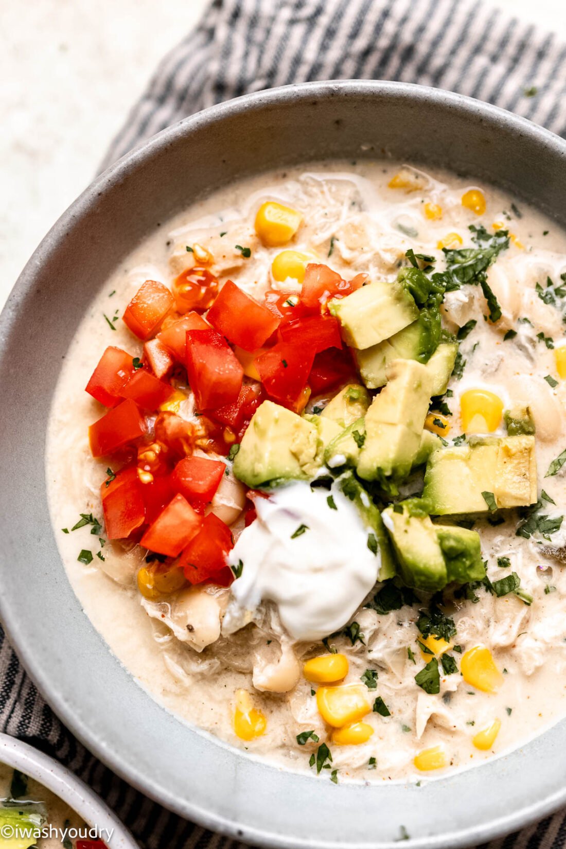 Cooked white chicken chili in bowl topped with avocado, sour cream, and tomatoes. 