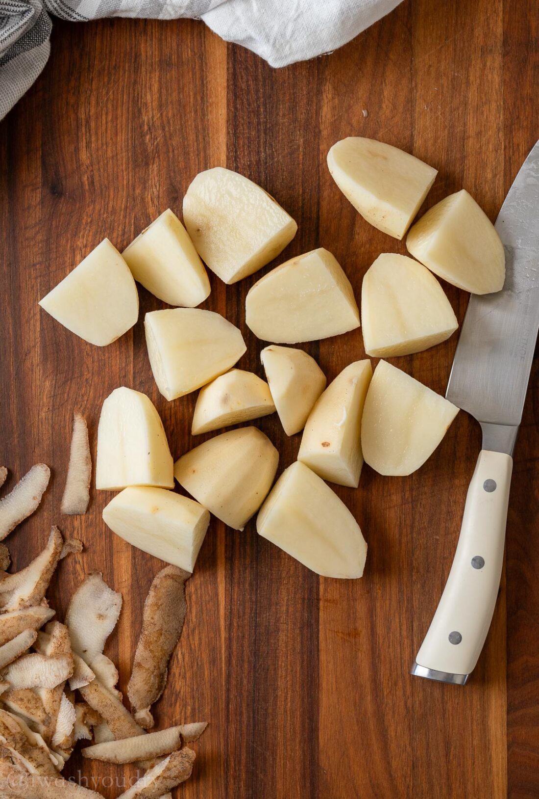 Peeled and quartered russet potatoes with knife on cutting board. 