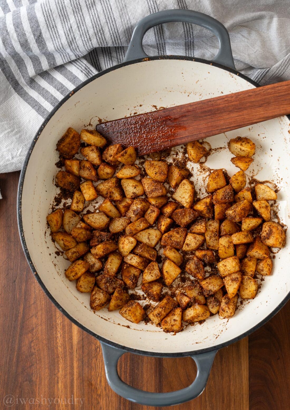 Cooking potatoes in frying pan with wooden spatula. 