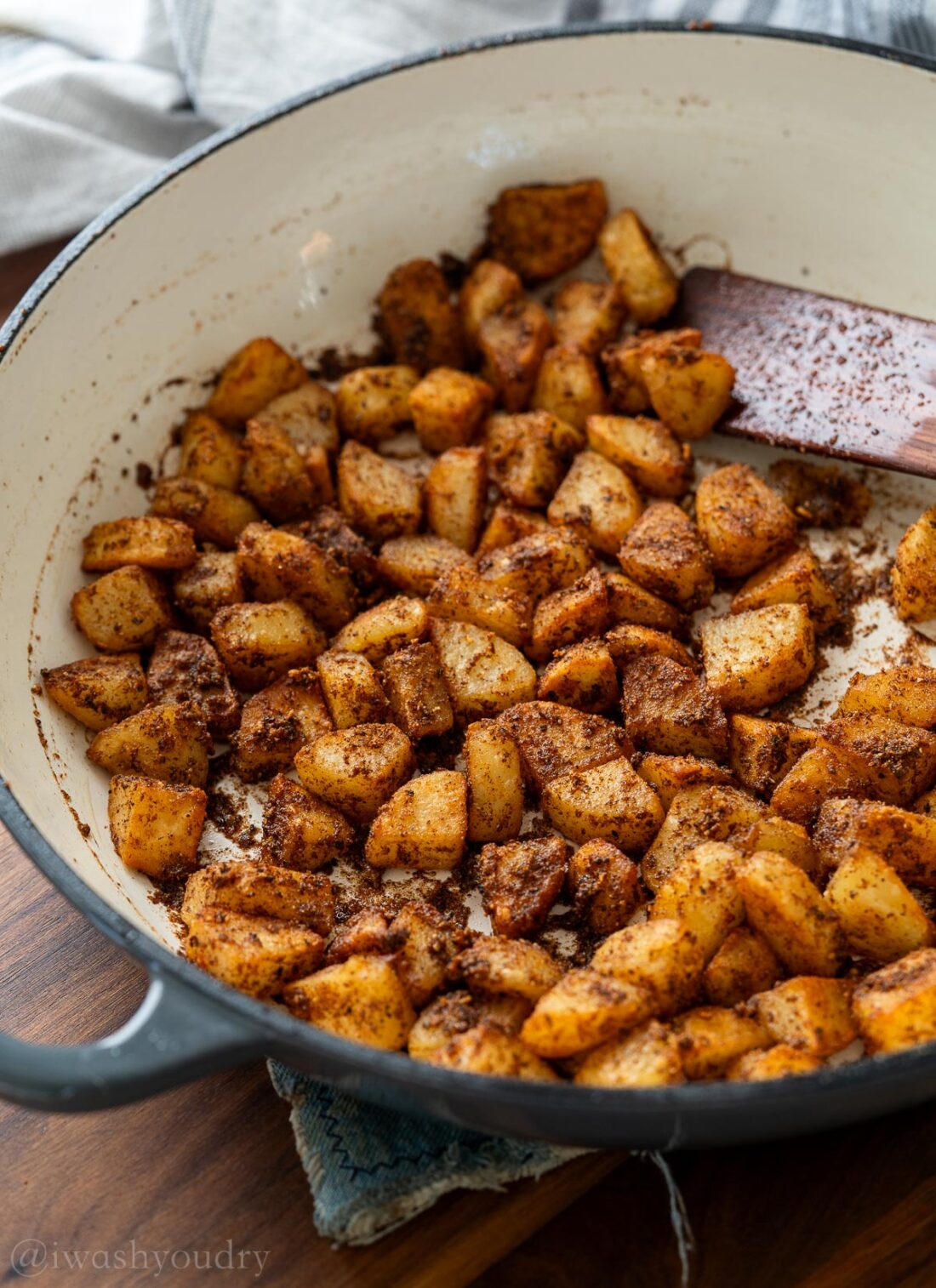 Crispy fried breakfast potatoes in white skillet with wood spatula. 