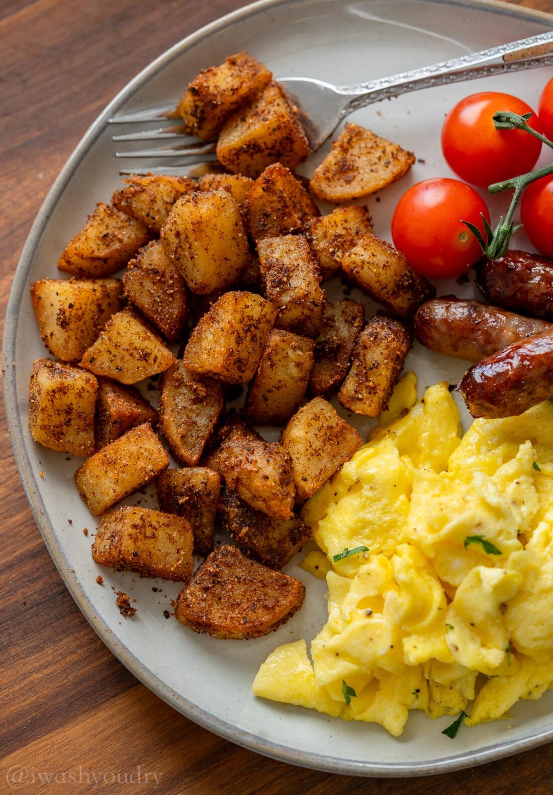 Scrambled eggs, potatoes, and sausage on a white plate. 