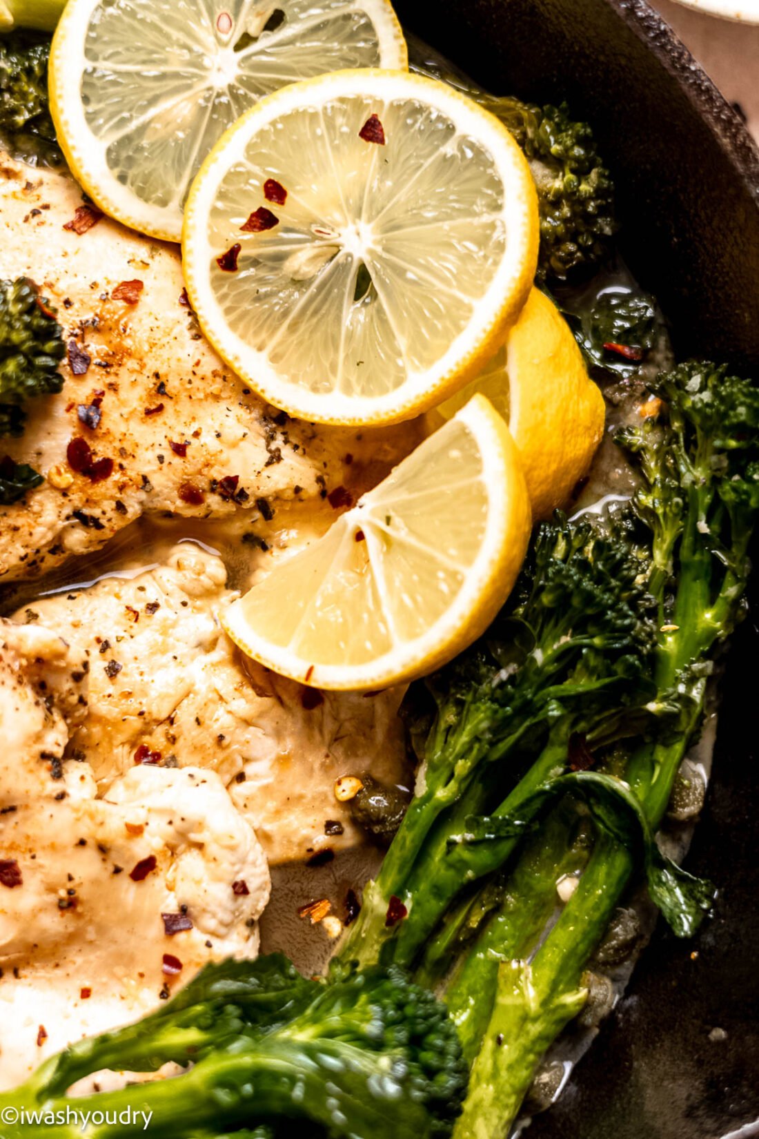 Cooked chicken and broccolini in frying pan with lemon slices and capers. 