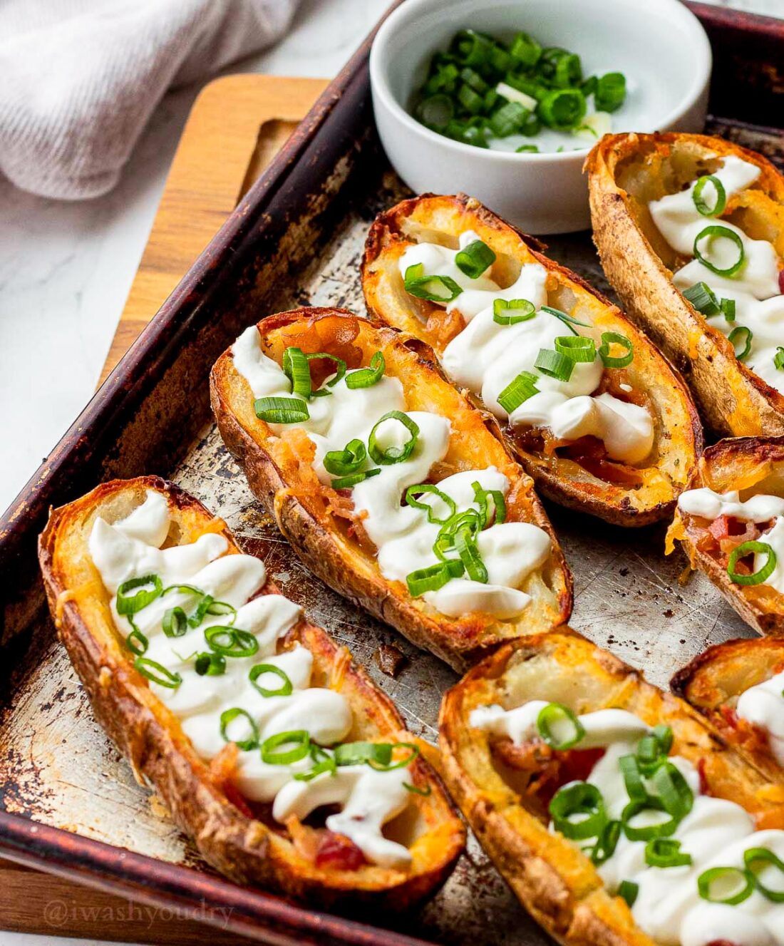 potato skins recipe filled with cheese, bacon and sour cream on metal tray.