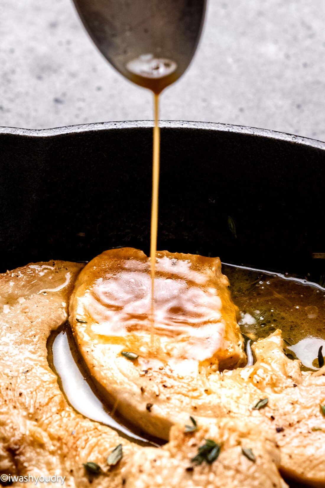 Spooning pan sauce over turkey cutlets with herbs in black pan.