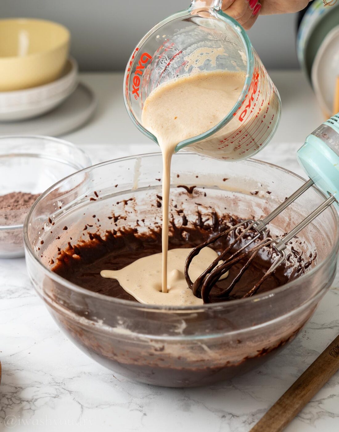 pouring buttermilk mixture with espresso powder into chocolate cake batter.