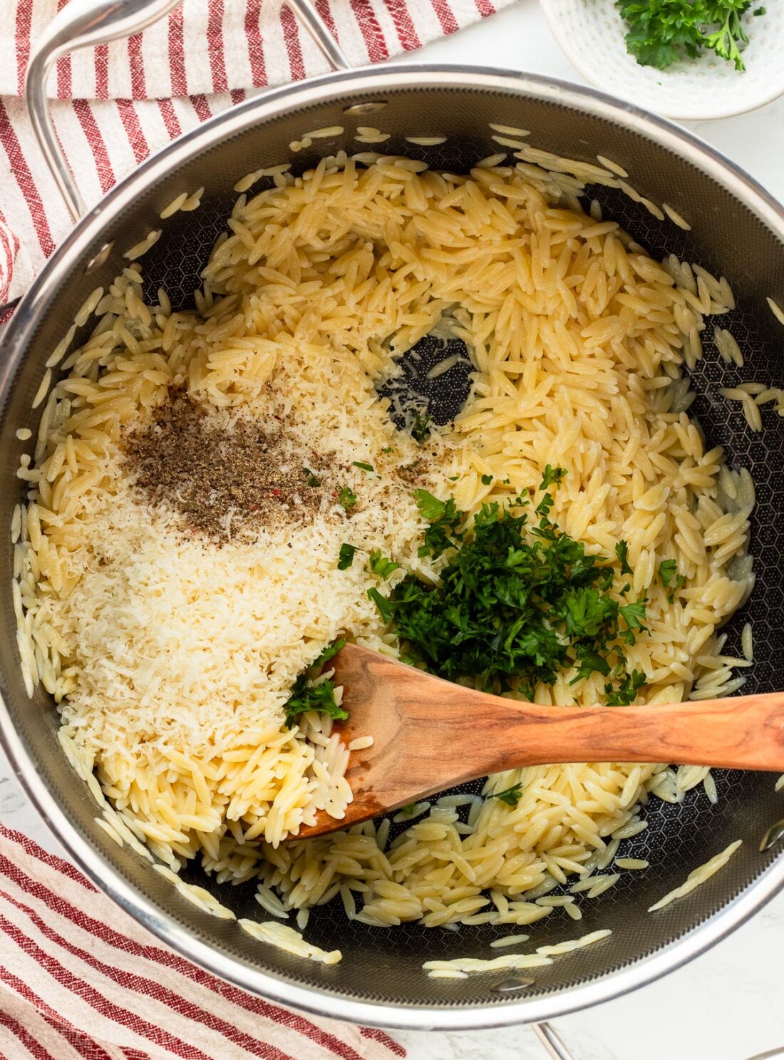 Unmelted butter in pot of cooked orzo pasta with parmesan and parsley.