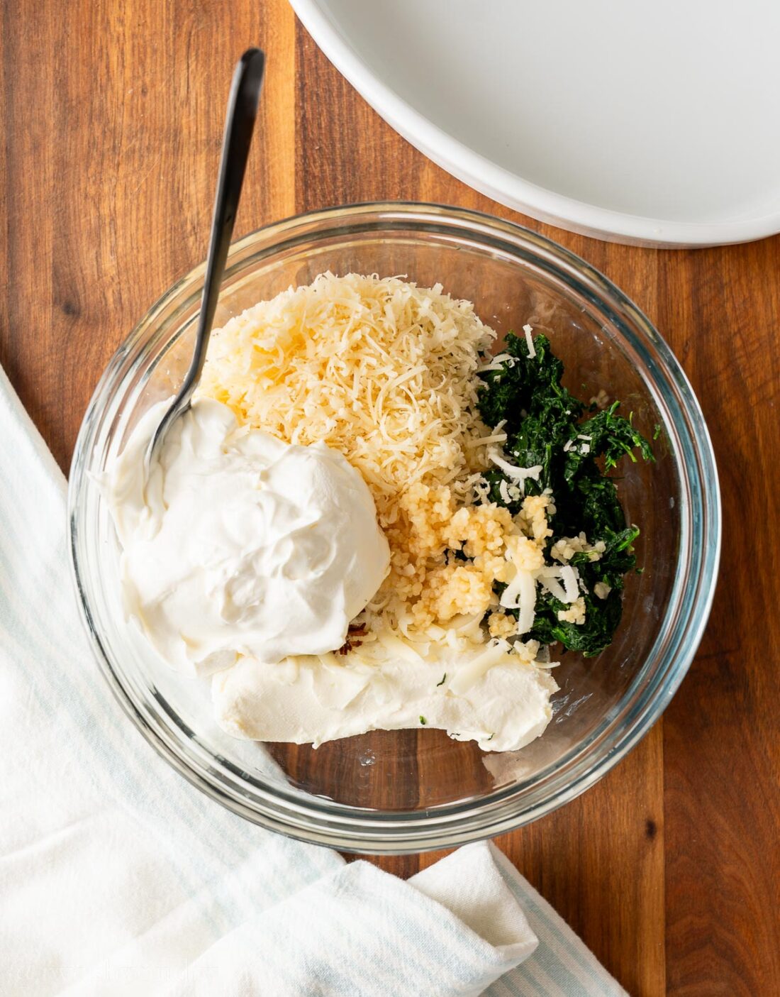 Cream cheese, sour cream and spinach in a glass bowl with mozzarella cheese and garlic.