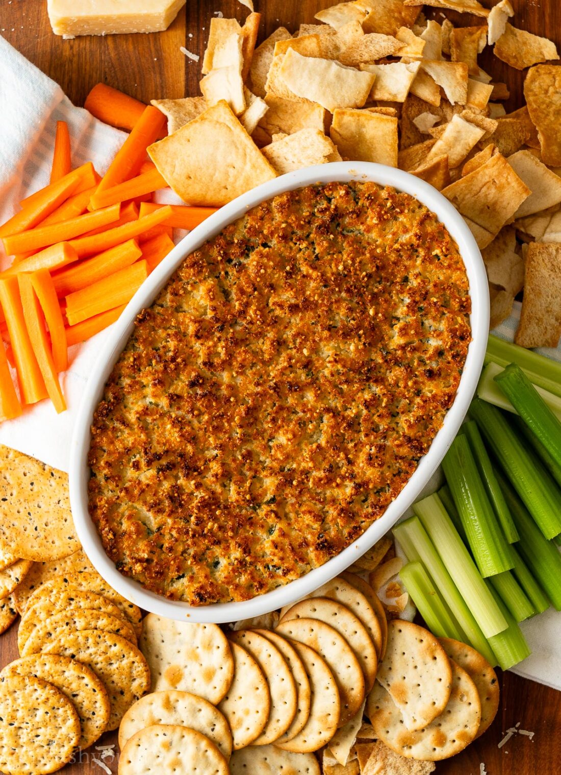 parmesan crusted spinach dip on serving platter with crackers, celery and carrots.