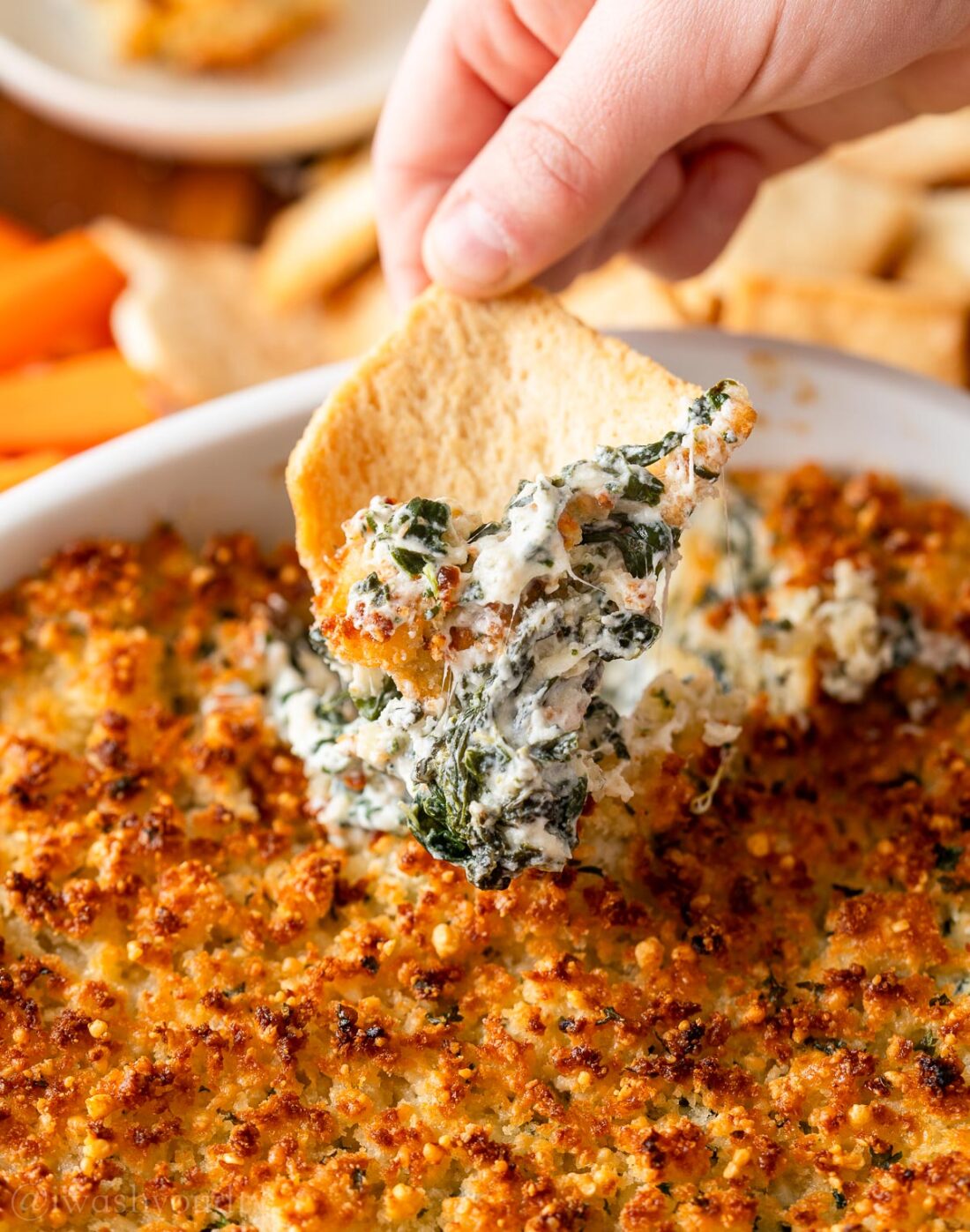 chip scooping up spinach dip in white dish.
