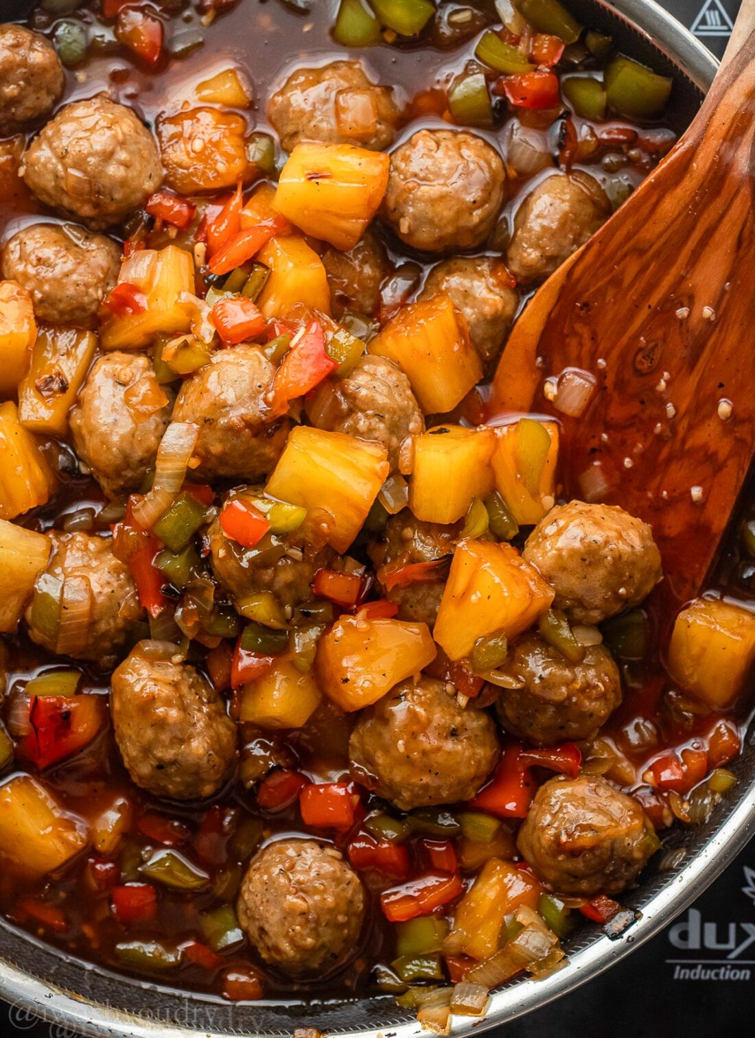sweet and sour meatballs in sauce with pineapples and peppers.