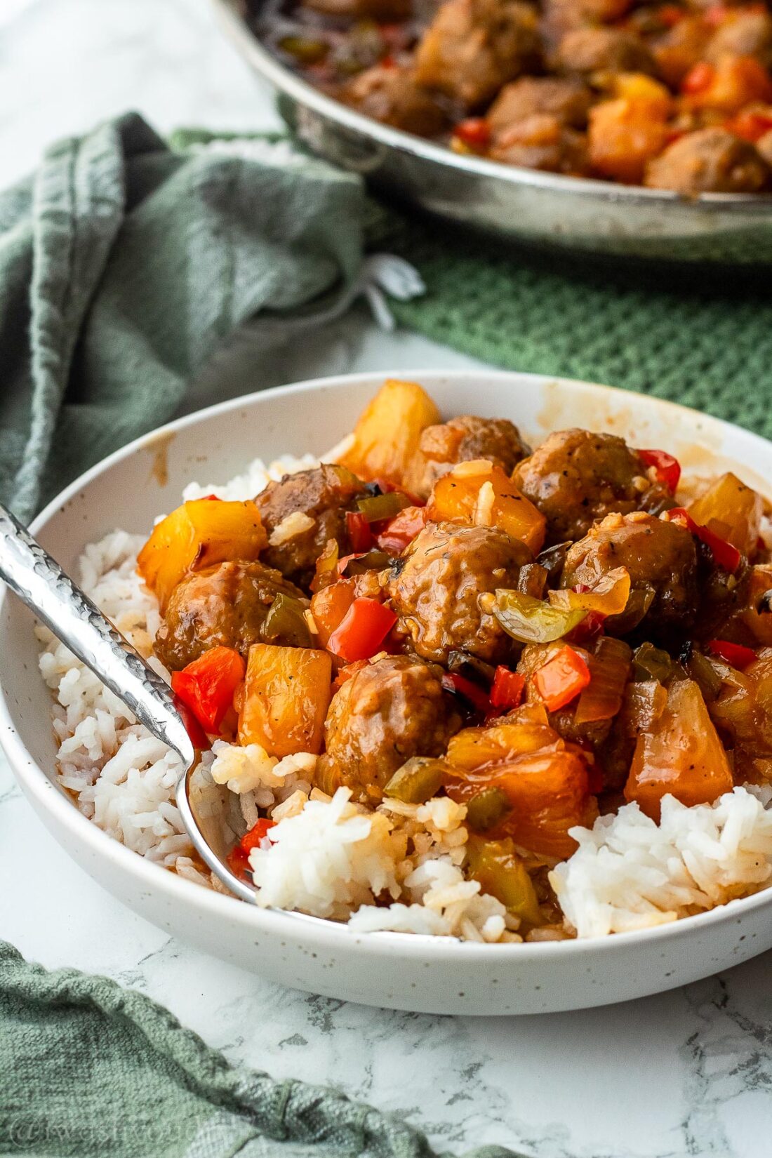 Bowl of cooked sweet and sour meatballs over white rice. 