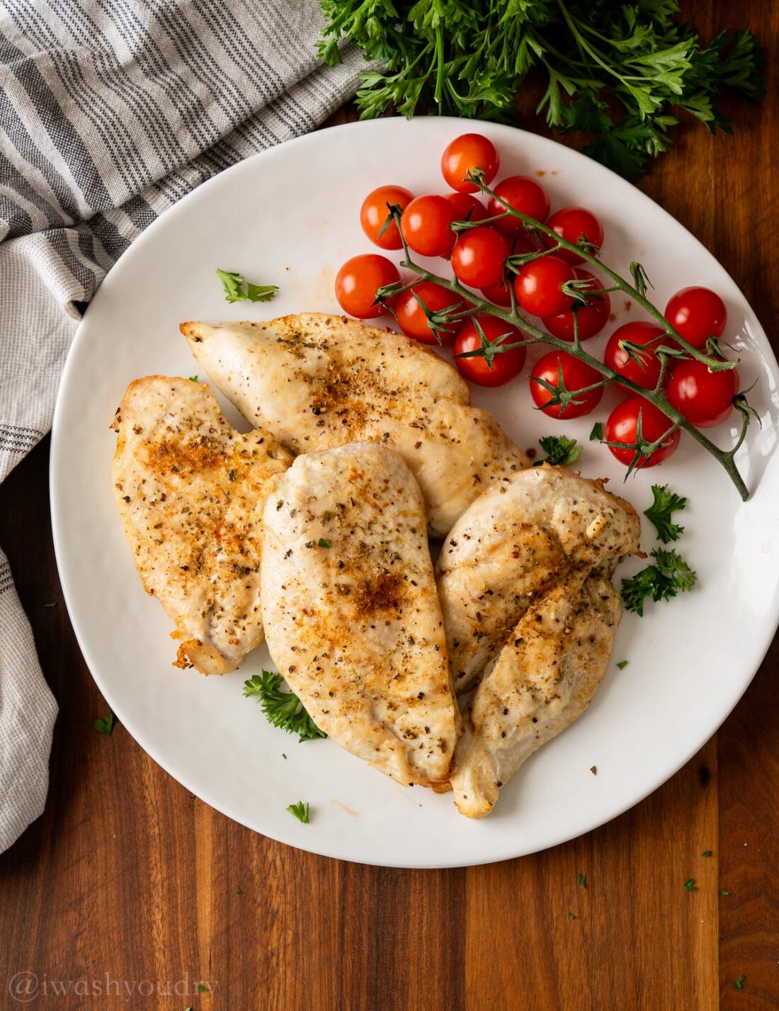Cooked chicken on white plate with vine tomatoes. 