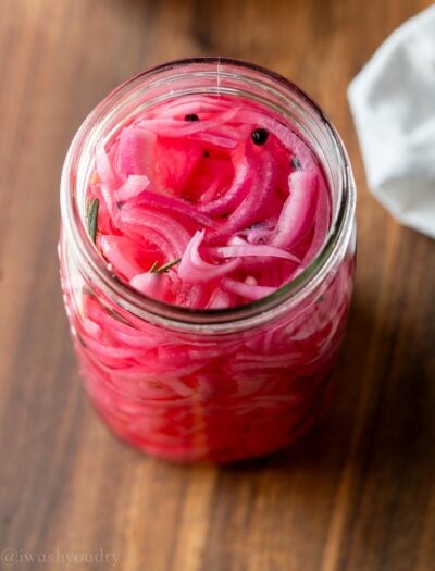 Pickled red onions in glass jar on wood cutting board.
